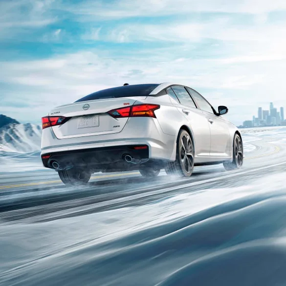 2027 Nissan Altima in white seen from behind driving in snowy landscape illustrating all-wheel drive at MATZ Nissan in Troy AL